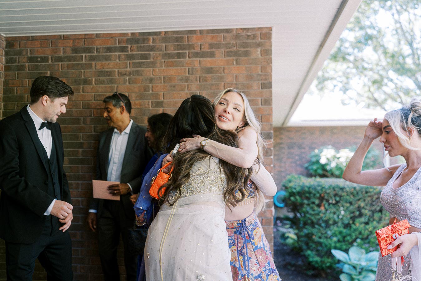 A diverse group of people engaging in a warm conversation and embracing outside, dressed in formal and festive attire, suggesting a celebratory occasion.