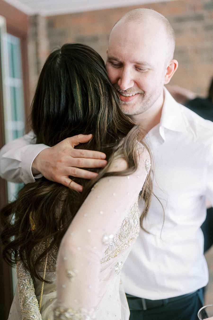 A man in a white shirt warmly embraces a woman with long dark hair, both smiling and sharing a joyful moment.