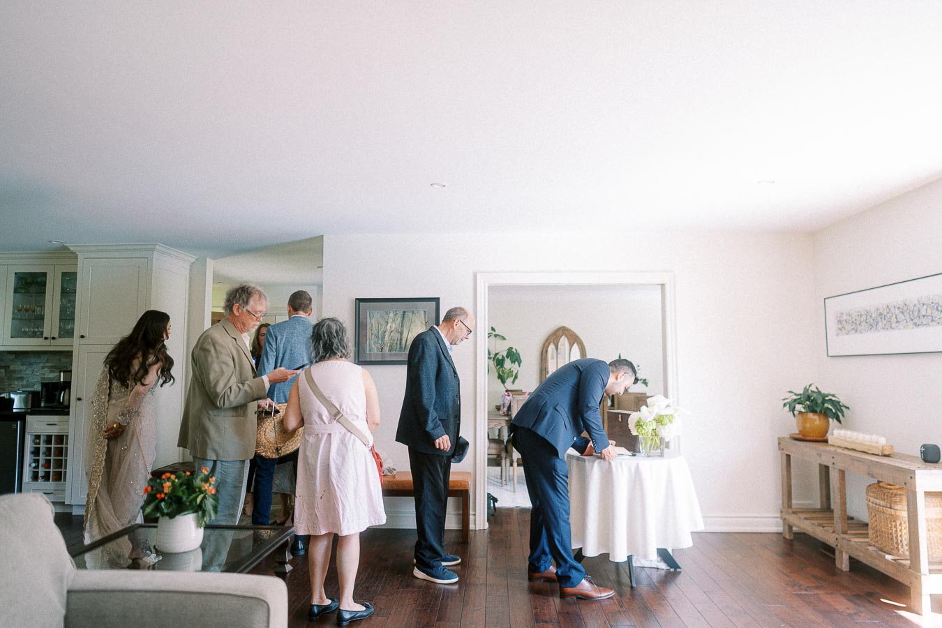 Guests signing a book at a gathering inside a modern living room with natural light, hardwood floors, and elegant decor.