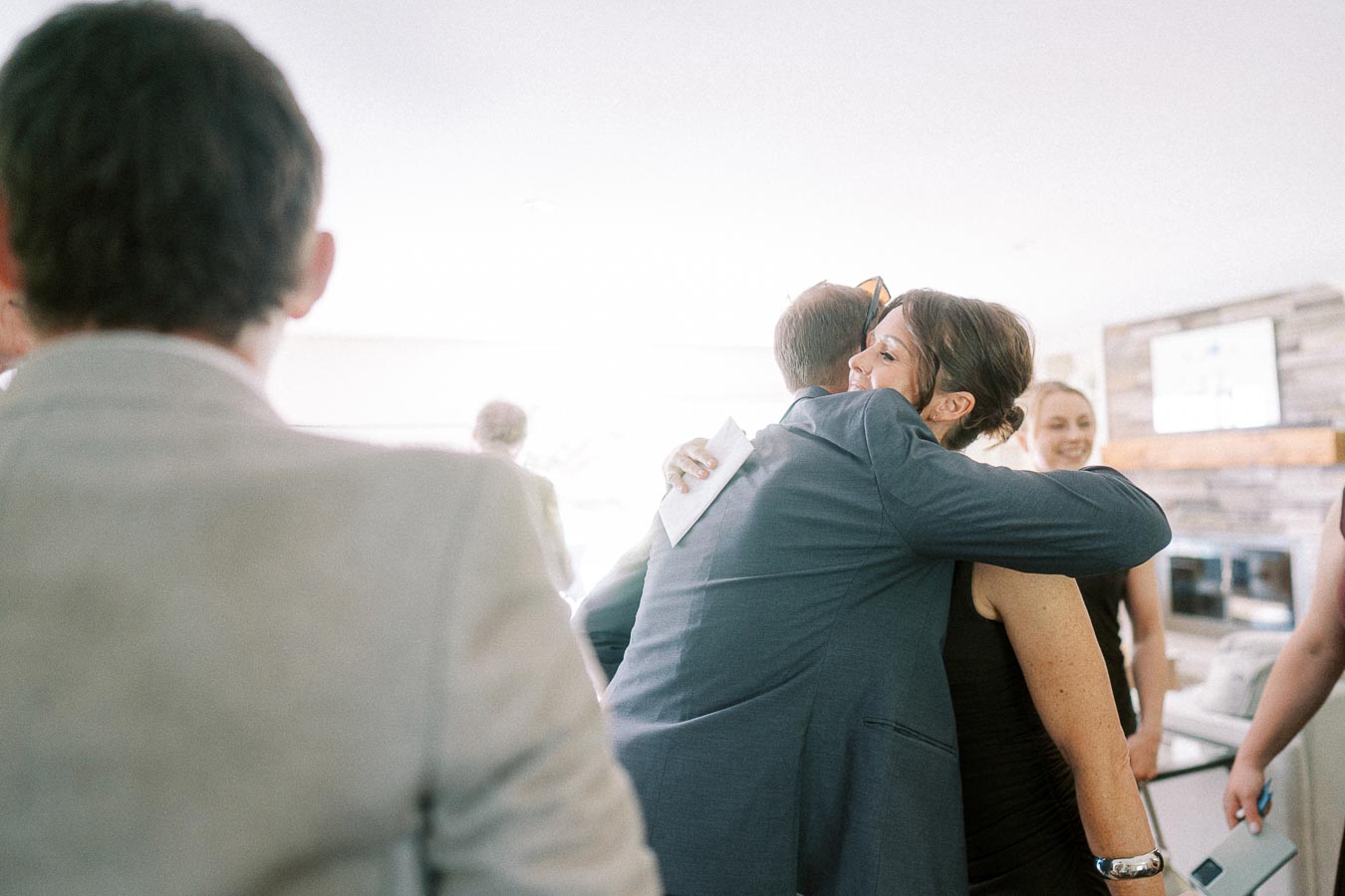 People sharing a warm hug at a social event indoors, with soft lighting and joyful expressions, capturing the essence of connection and celebration.