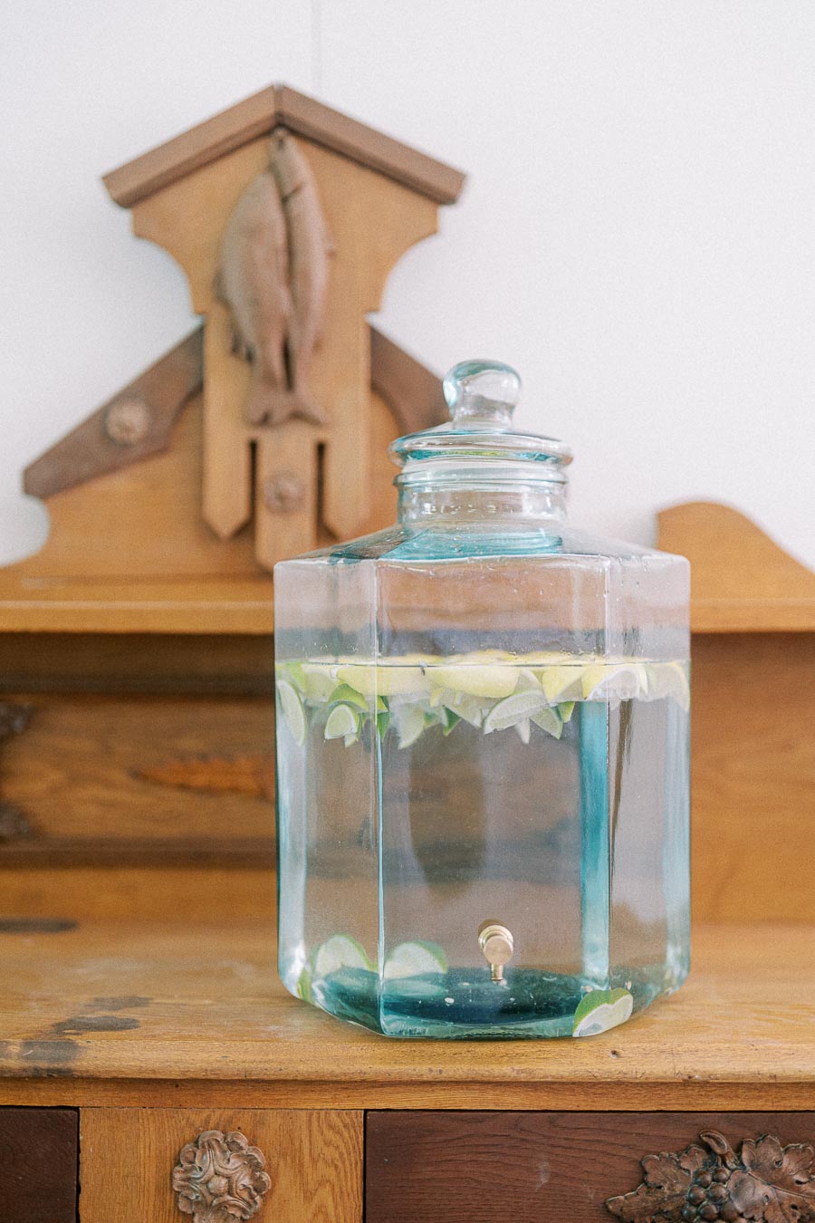 Glass jar filled with lemon and lime infused water, placed on a rustic wooden cabinet adorned with decorative accents in a cozy home setting.