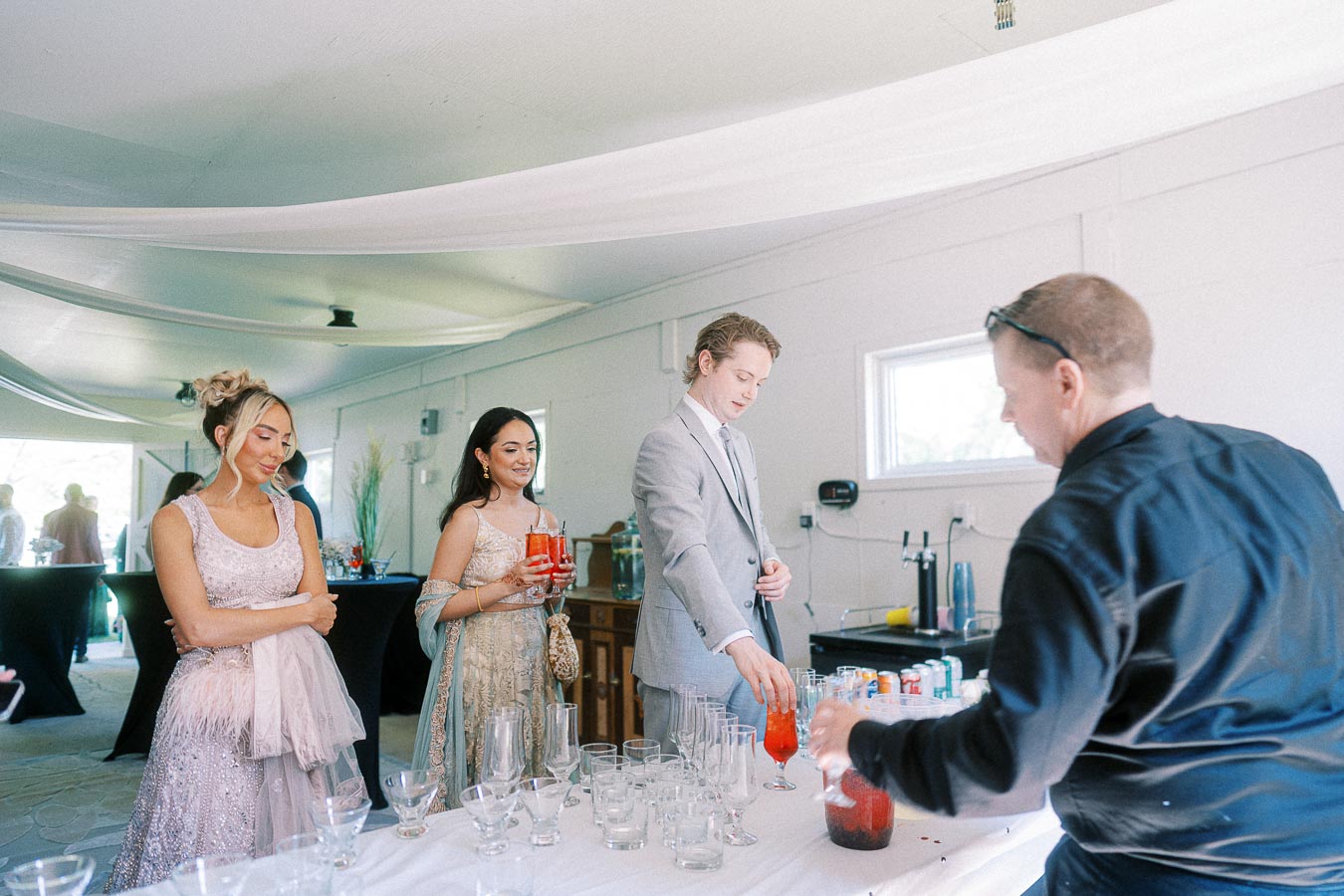 Elegant event with guests in formal attire at a drink station, featuring mixed beverages, in a bright indoor setting.