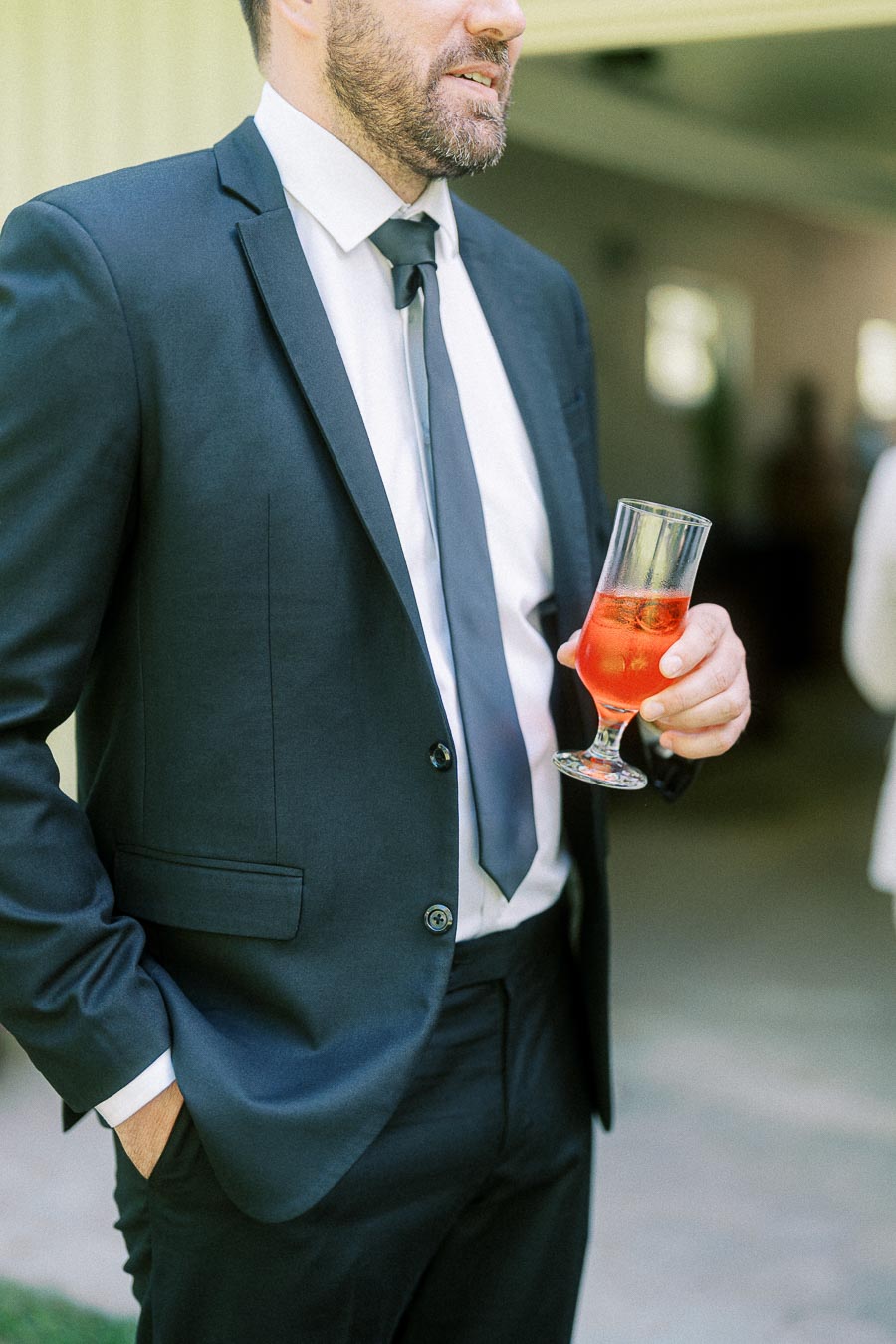 A man in a dark suit and tie holding a glass of a red cocktail at a formal event.