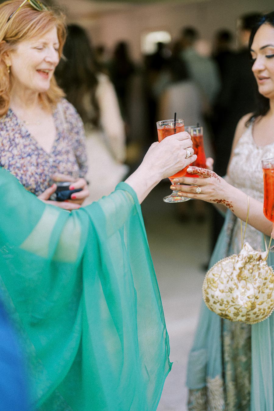 Women in elegant dresses toasting with red cocktails at a social gathering, highlighting festive celebration and camaraderie.