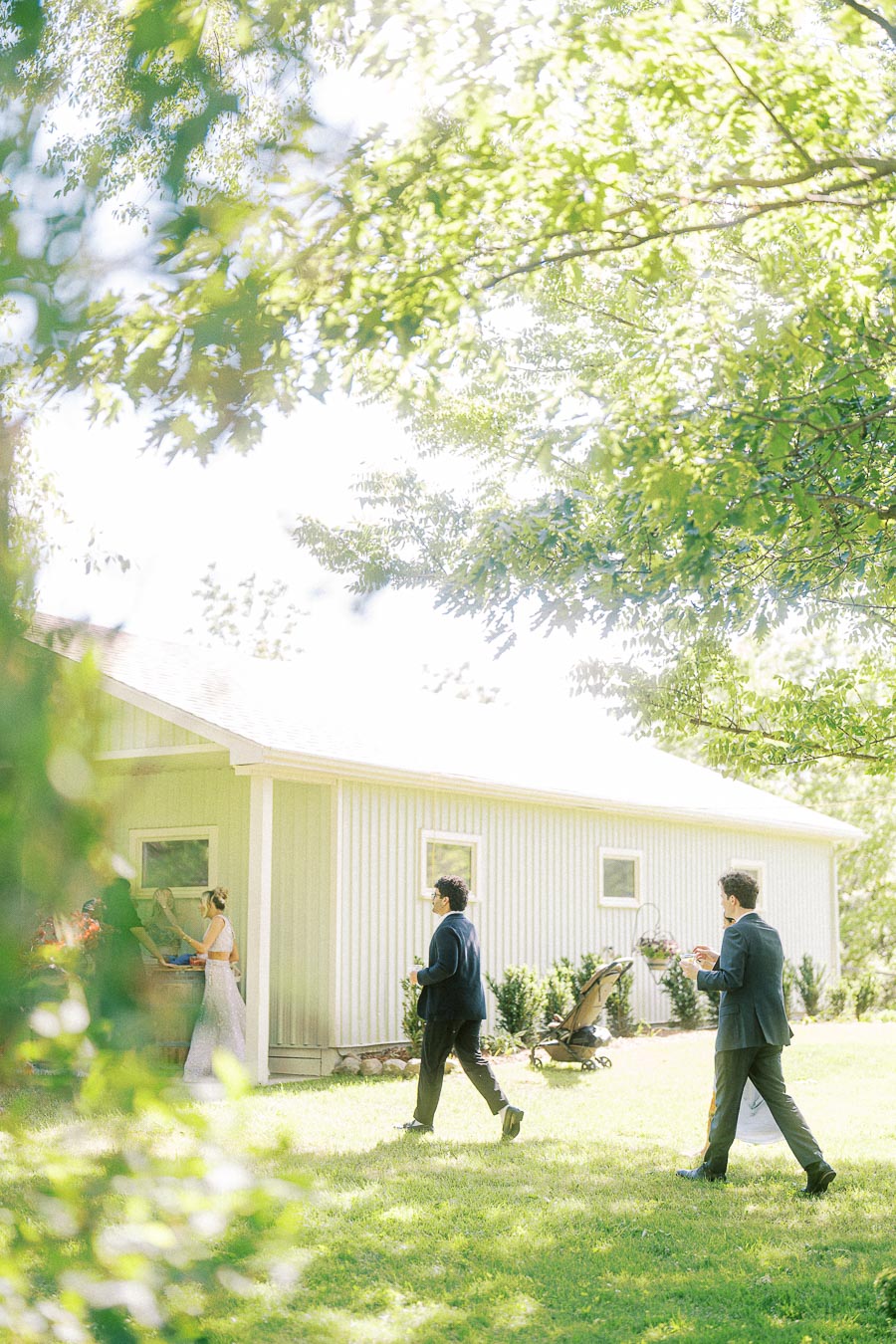 A serene outdoor scene with a few people on a grassy lawn near a light-colored building, surrounded by lush green trees.