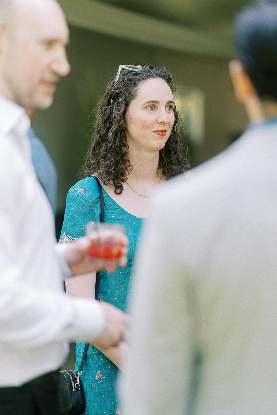 A woman in a teal dress engaging in conversation at an outdoor social event, surrounded by other attendees.
