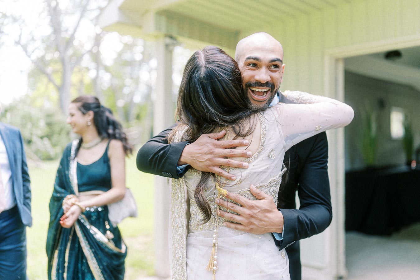 Two people embracing joyfully at an outdoor event, with others in festive attire in the background.
