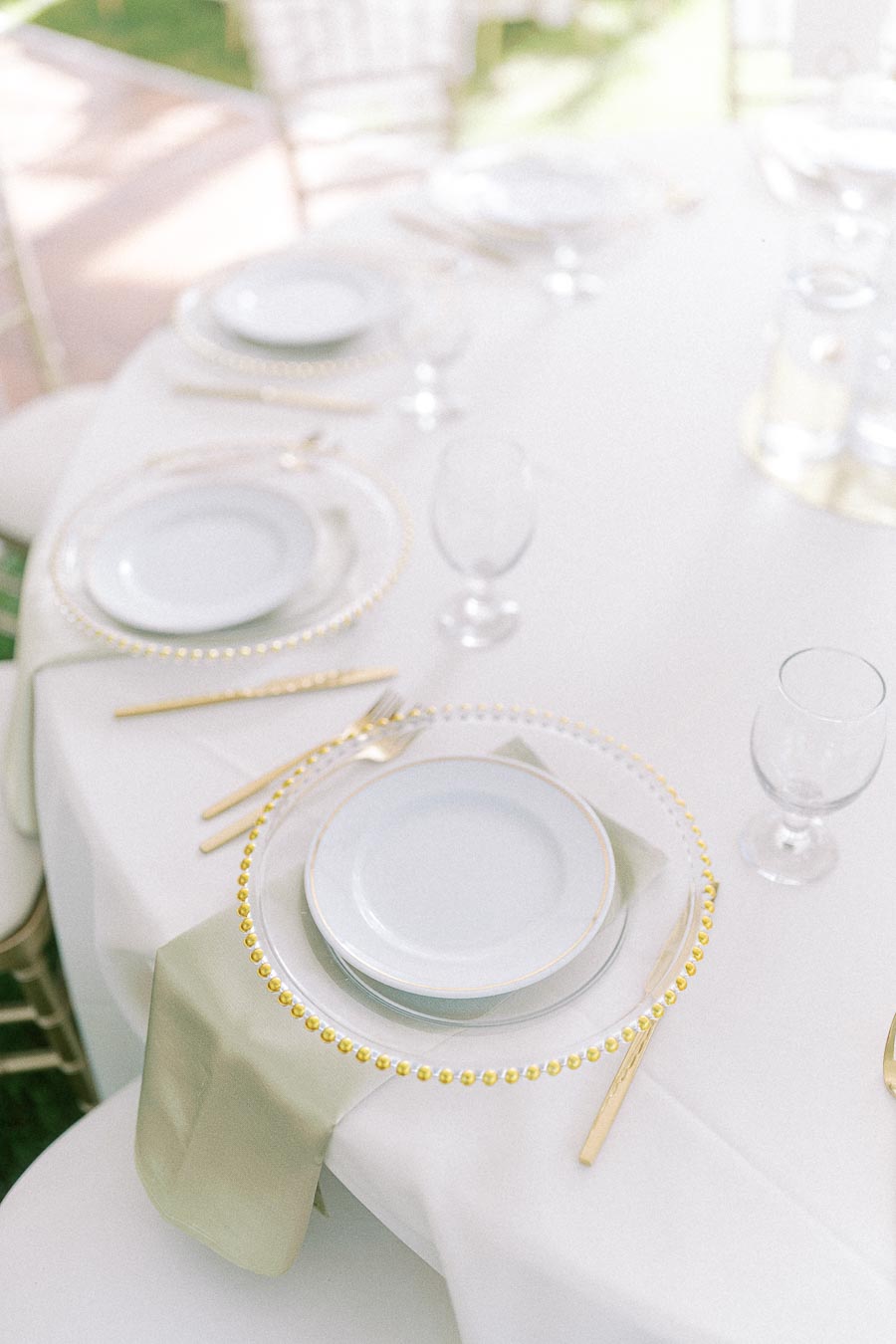 Elegant table setting with white plates and gold utensils on a round table with a white tablecloth and green napkins, ideal for weddings or formal events.
