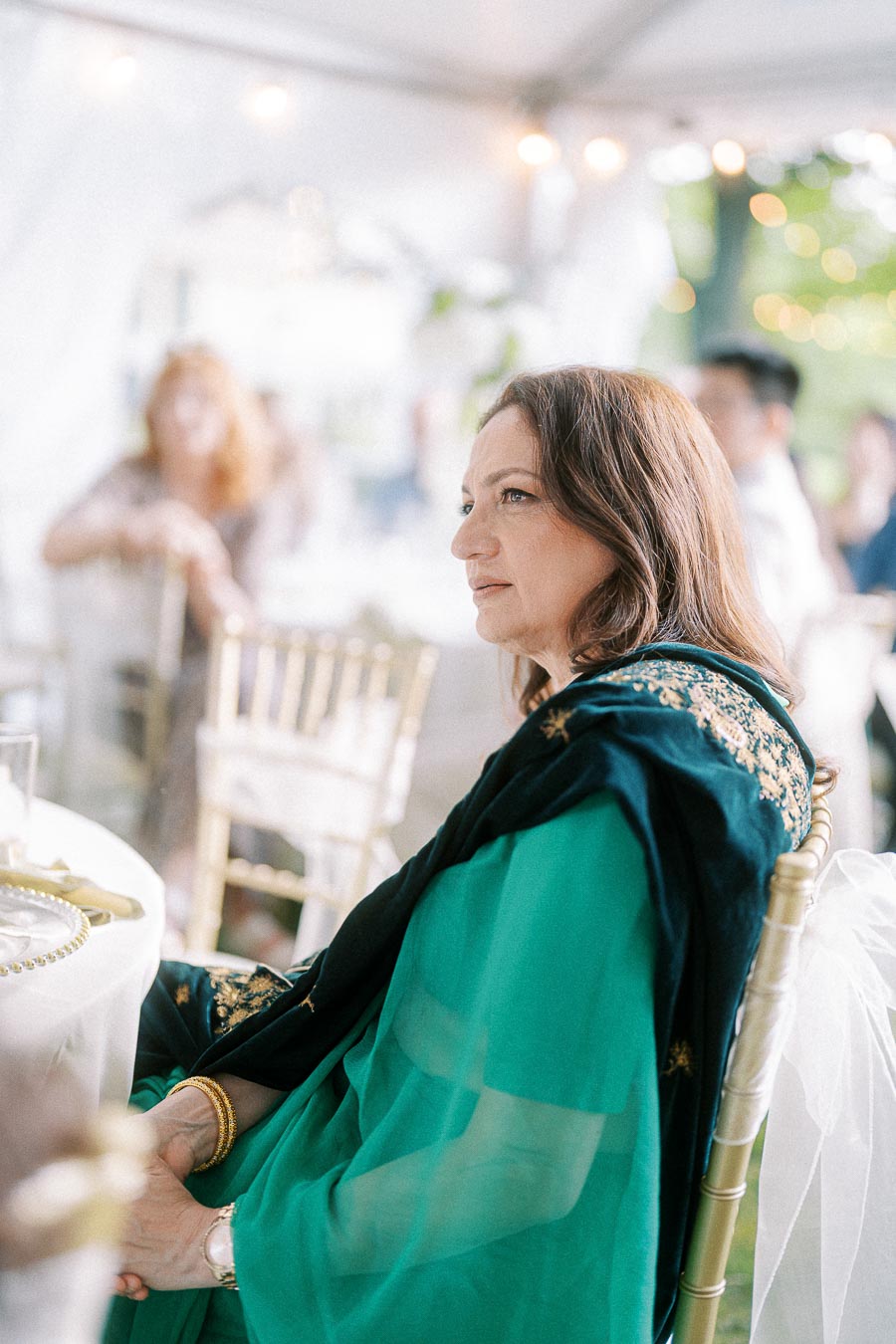 Elegant woman in a green and black saree sitting at a decorated table during an outdoor event.