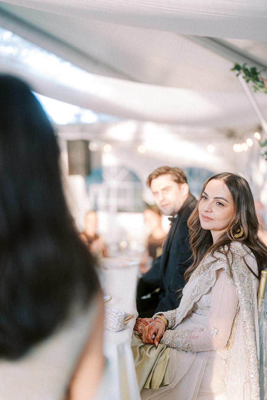 Elegant couple in formal attire attending a wedding event under a beautifully decorated canopy, featuring soft lighting and a romantic atmosphere.
