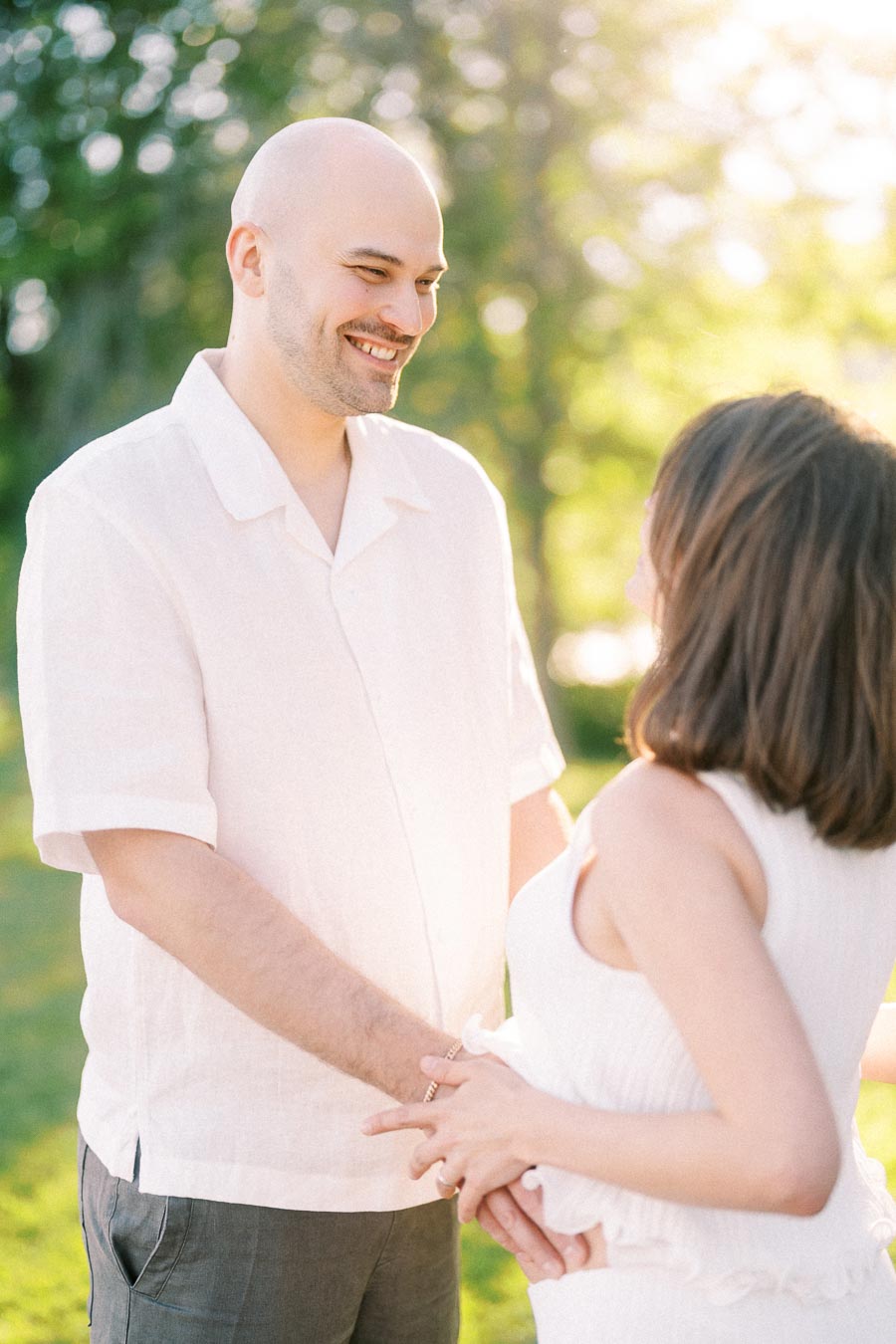 Expectant couple holding hands outdoors in warm sunlight during a maternity portrait.
