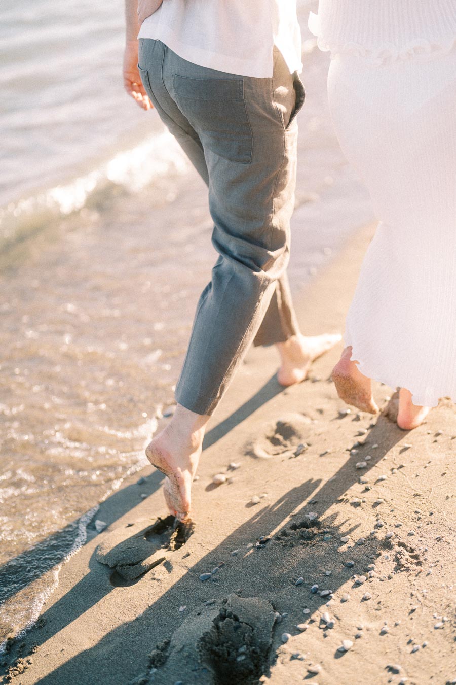 Barefoot couple walking along a sandy Lake Ontario shoreline in warm sunlight.