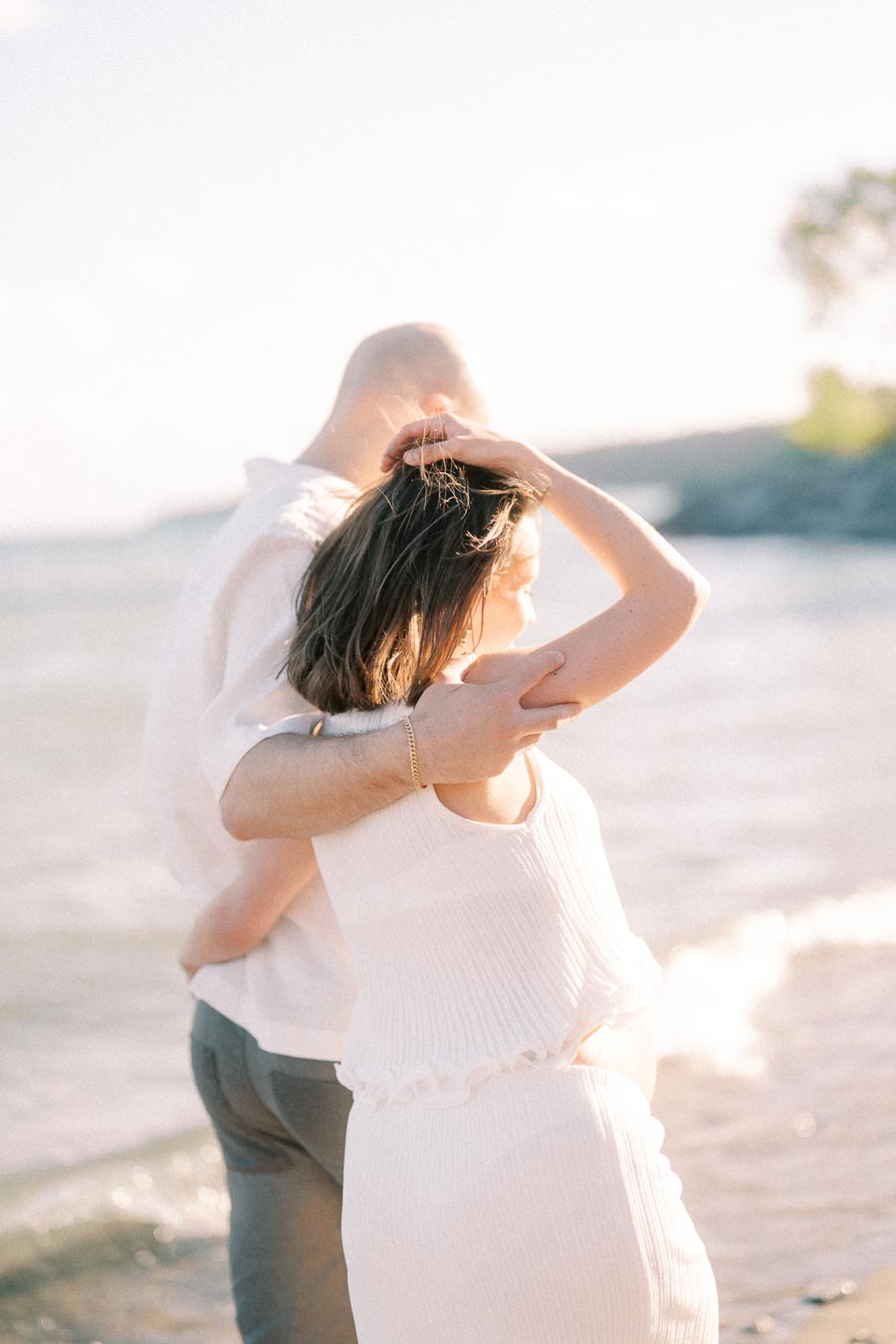 Expectant couple embracing by the water in soft backlight at Scarborough Bluffs.