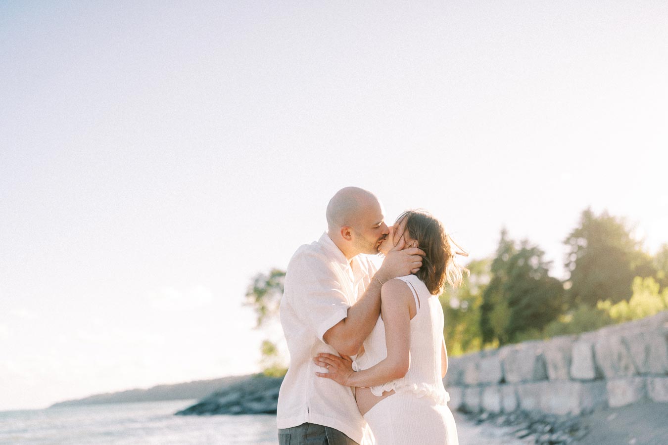 Expectant couple kissing by the water in soft evening light at Scarborough Bluffs.