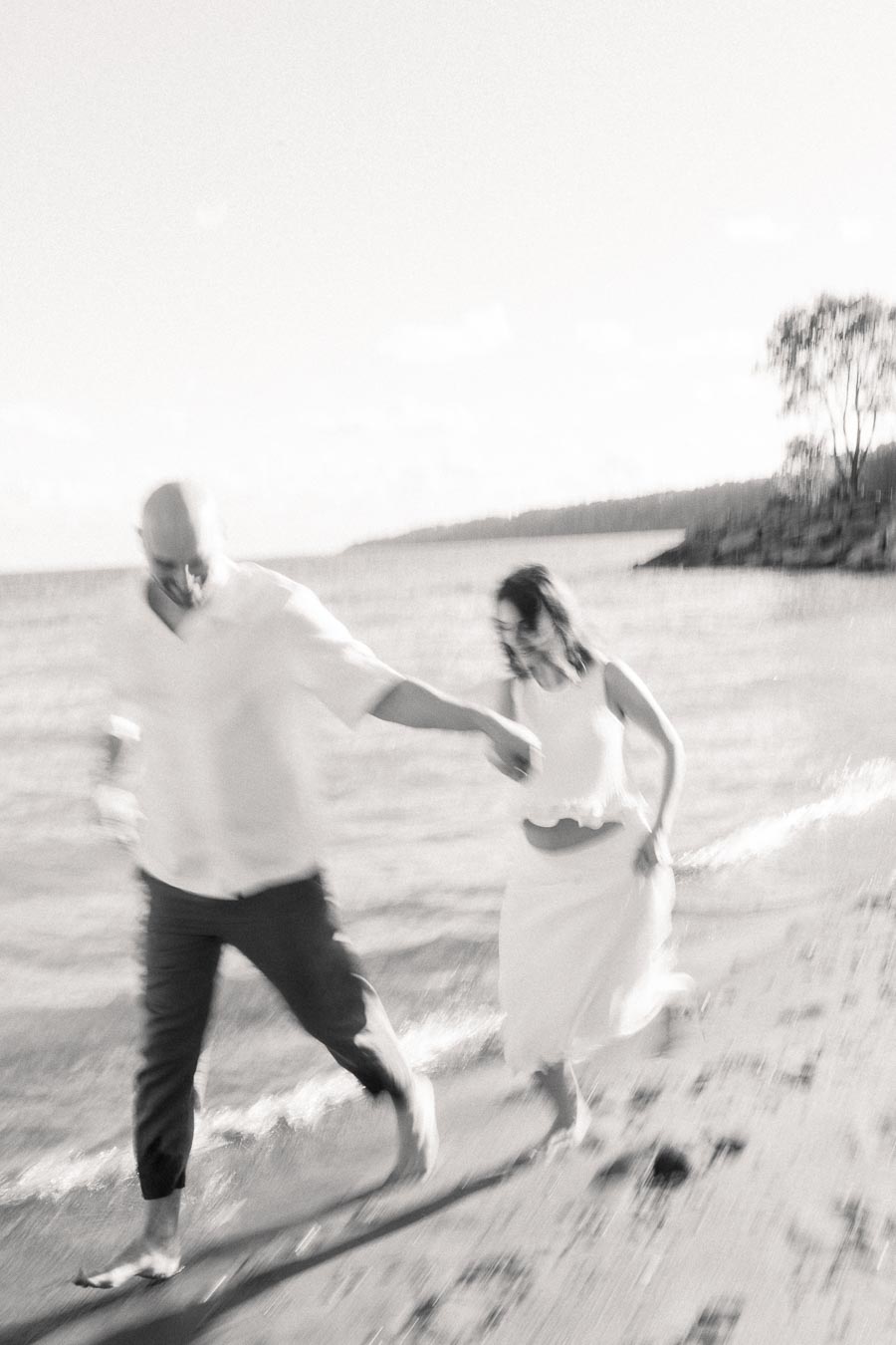 Expectant couple holding hands while running barefoot along the Lake Ontario shoreline.