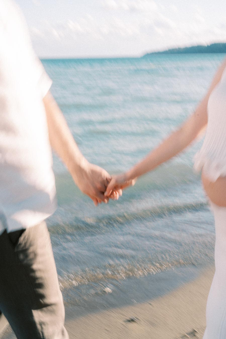 Expectant couple holding hands while walking beside the Lake Ontario shoreline.