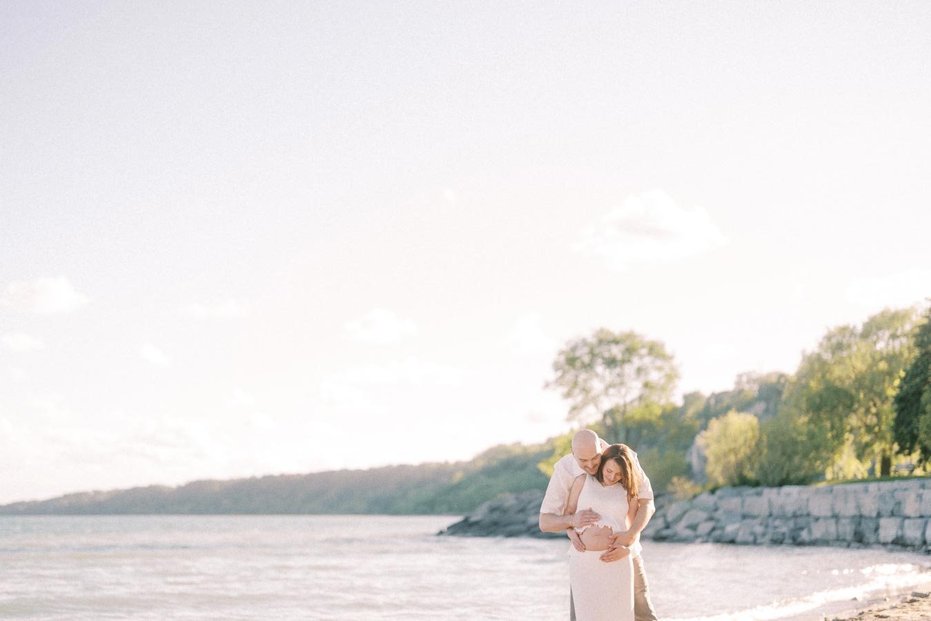 Expectant couple standing by Lake Ontario with hands on the baby bump at Scarborough Bluffs.