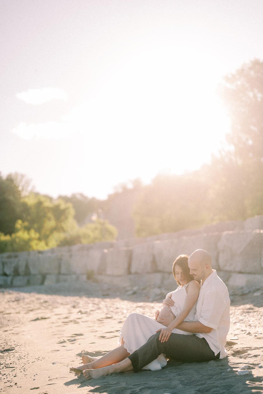 Pregnant couple sitting together on a sandy beach in warm evening light.