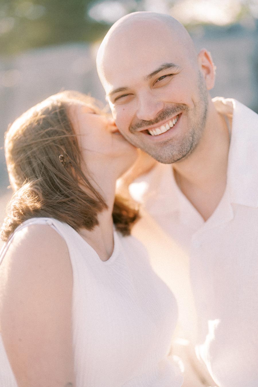 Pregnant woman kisses smiling partner on the cheek in warm backlight.