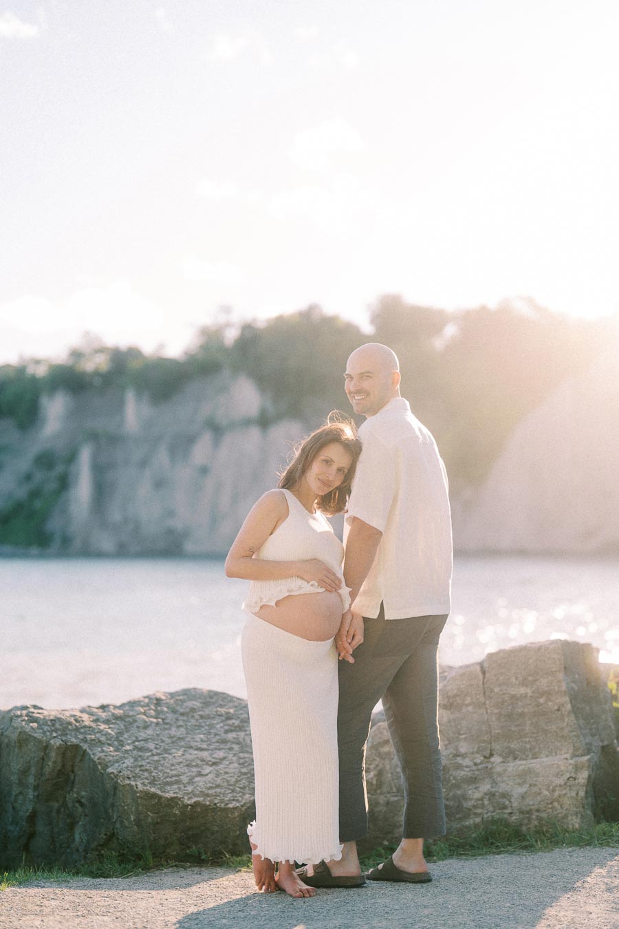 Pregnant woman and partner standing hand in hand by Lake Ontario at Scarborough Bluffs.