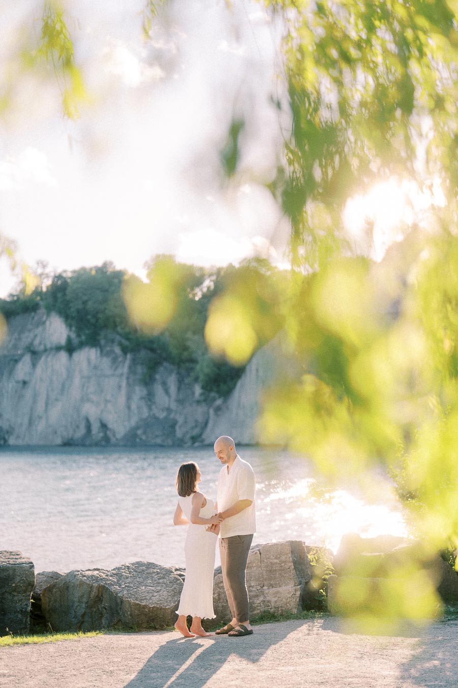 Expectant couple holding hands by Lake Ontario with Scarborough Bluffs in the background.