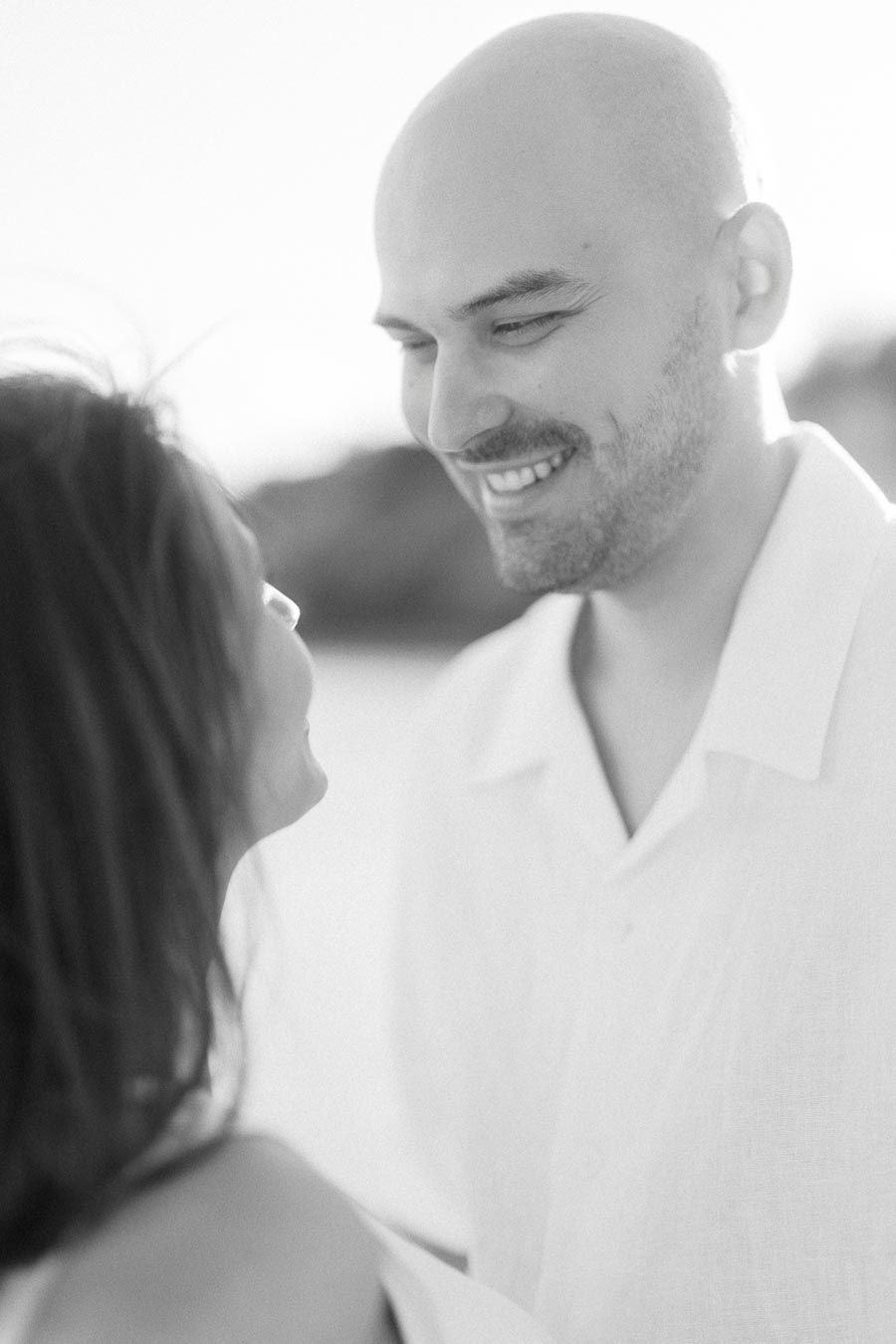 Black and white close-up of a smiling couple looking at each other outdoors.