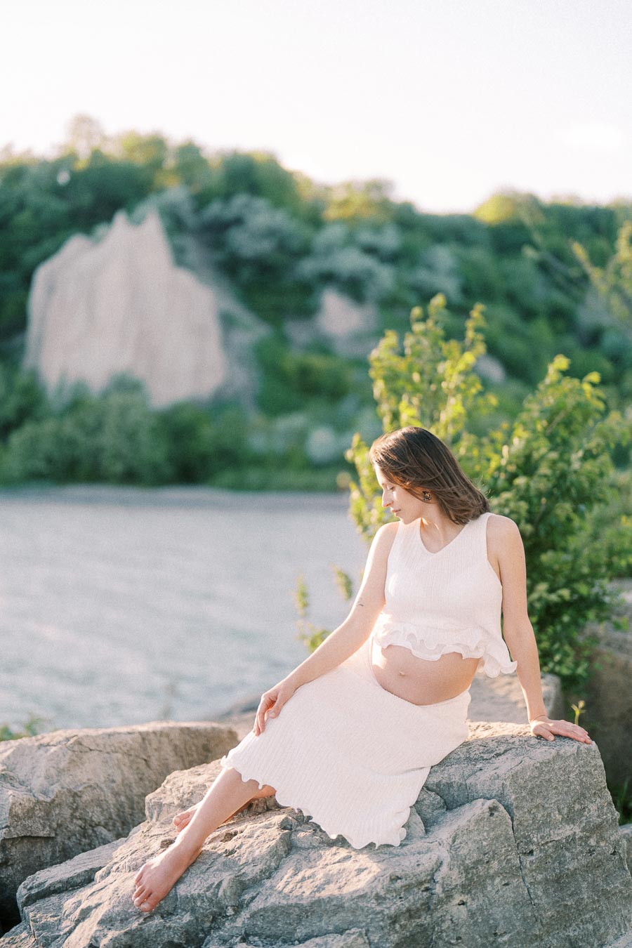 Pregnant woman in a white outfit sitting on rocks near Scarborough Bluffs.