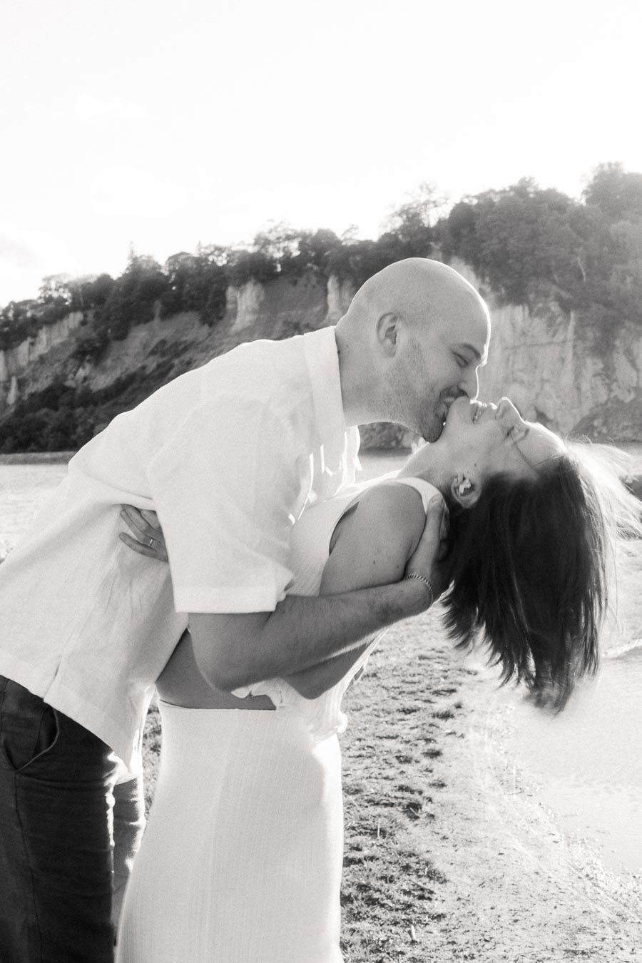 Black-and-white photo of a couple kissing as he dips her beside the Scarborough Bluffs shoreline.