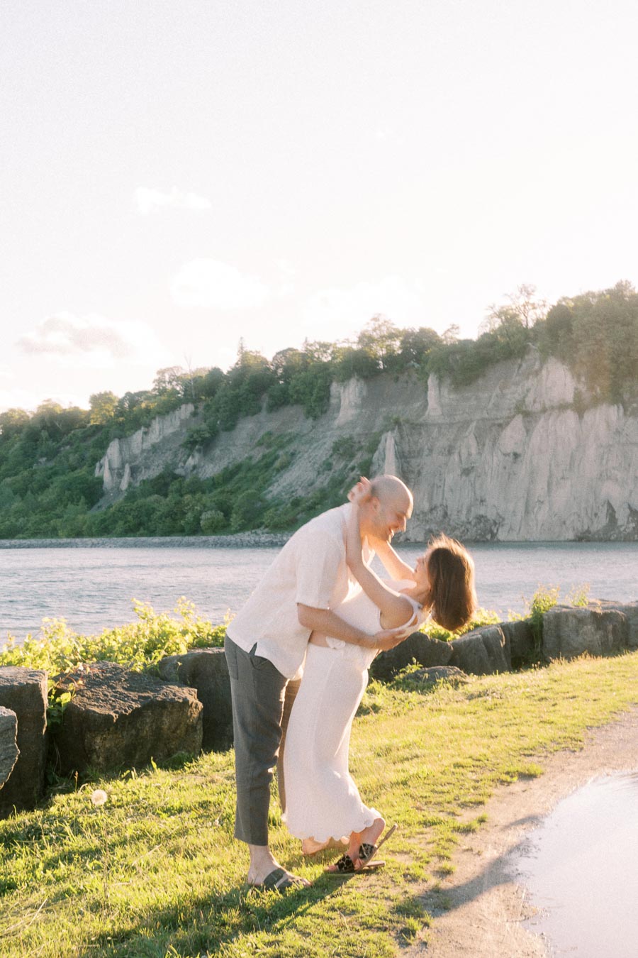 Expectant couple kissing by Lake Ontario with Scarborough Bluffs cliffs in the background.