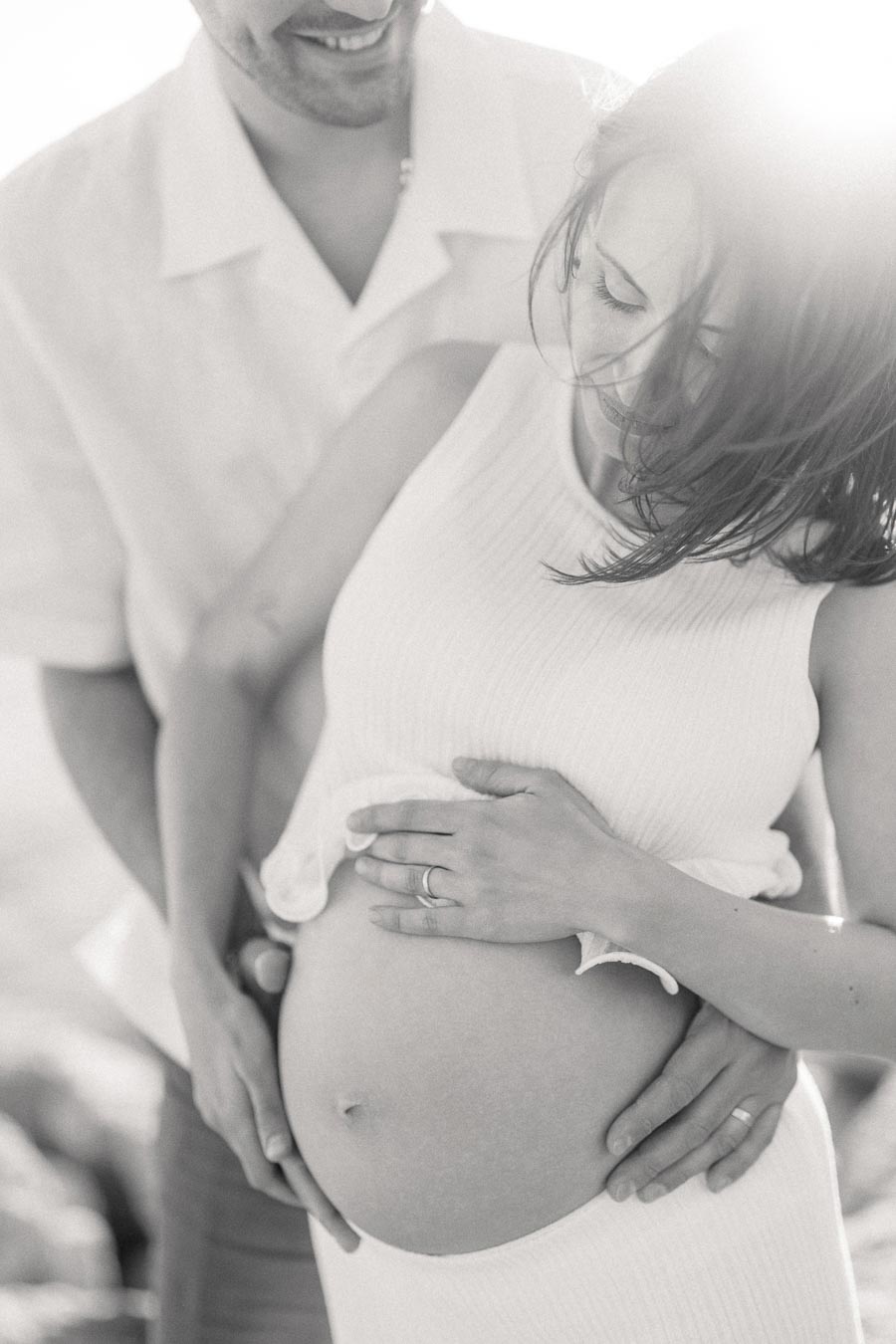 Black and white close-up of a pregnant woman with her partner holding her belly.