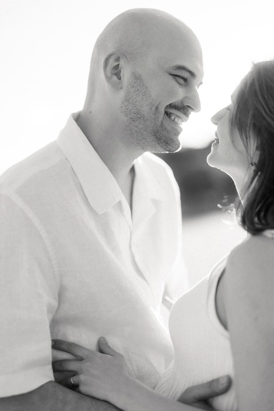 Black and white close-up of an expectant couple smiling face to face outdoors.