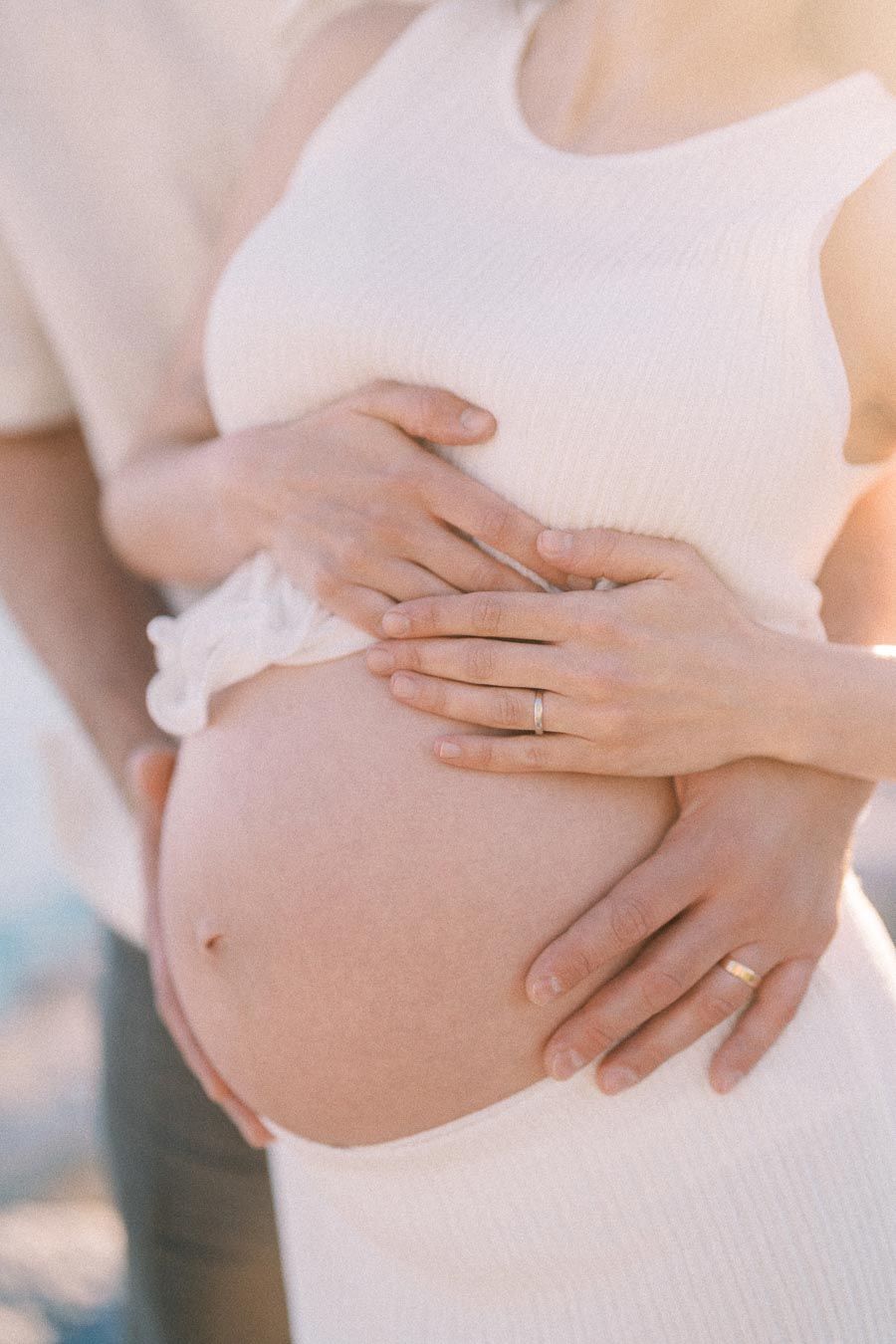 Close-up of expectant parents holding a pregnant belly with wedding rings visible.