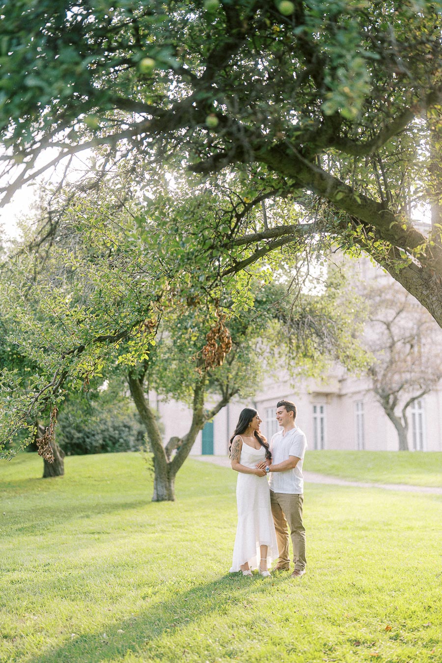Couple standing beneath orchard trees during Dundurn Castle engagement photoshoot
