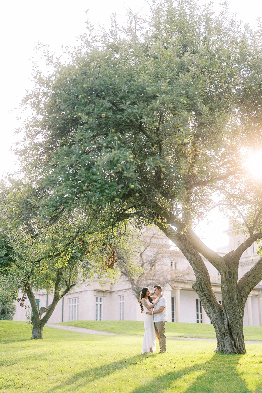 Couple embracing under sunlit trees at Dundurn Castle in Hamilton