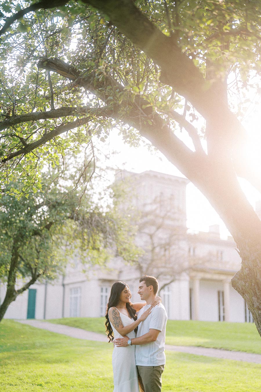 Couple embracing beneath sunlit trees at Dundurn Castle in Hamilton