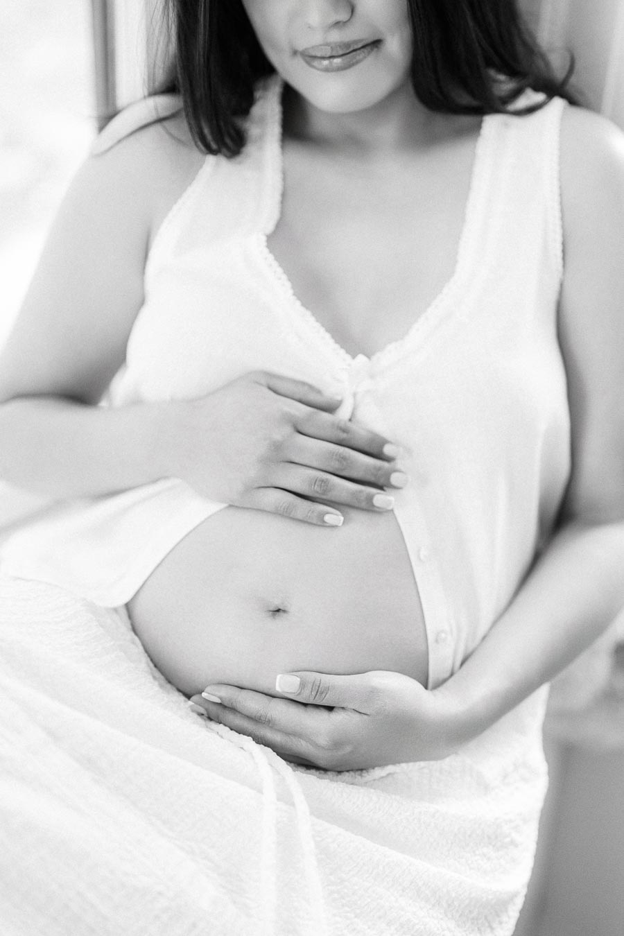 Black and white maternity portrait with hands resting on a pregnant belly.