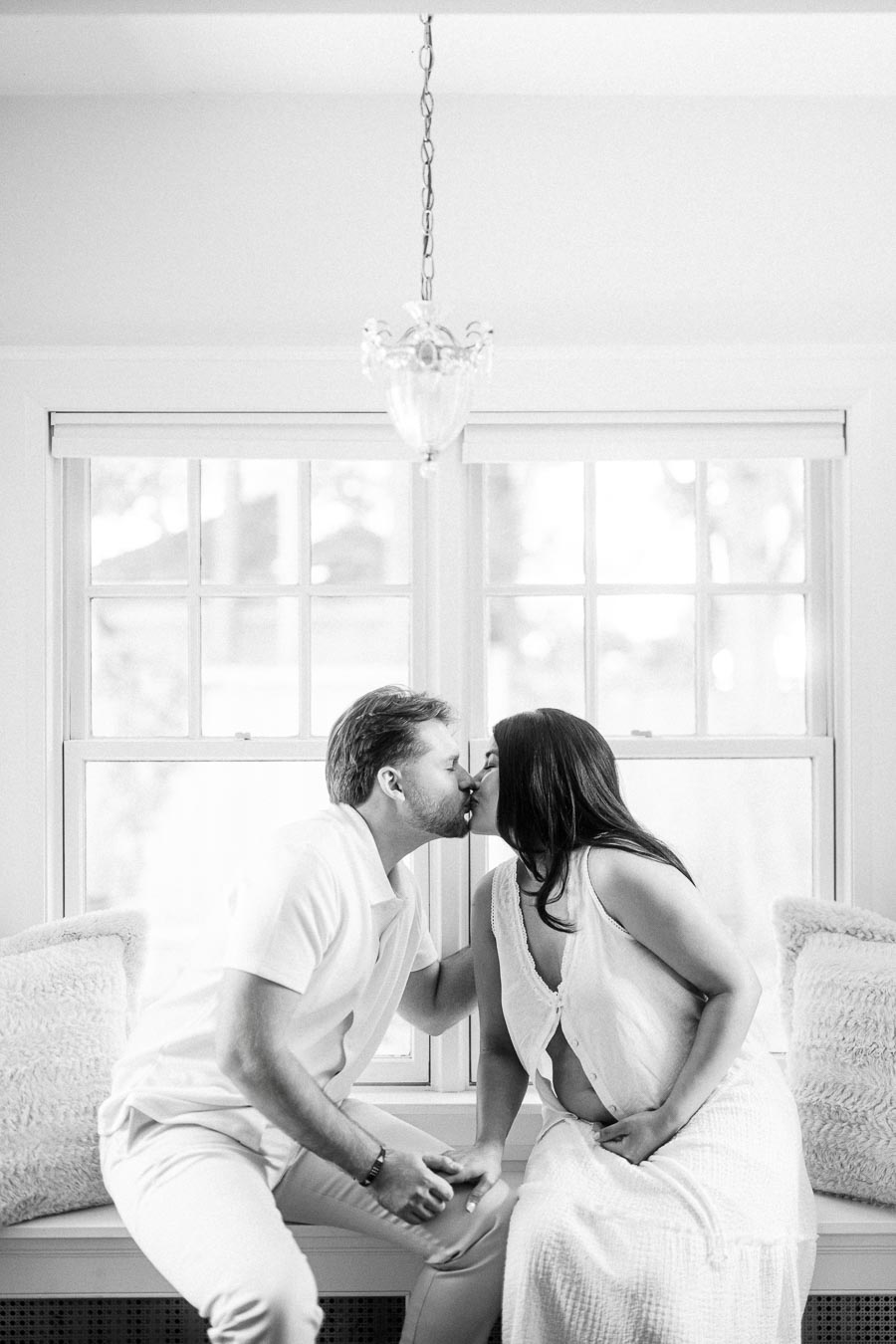 Couple kissing while seated on a bright window bench indoors.