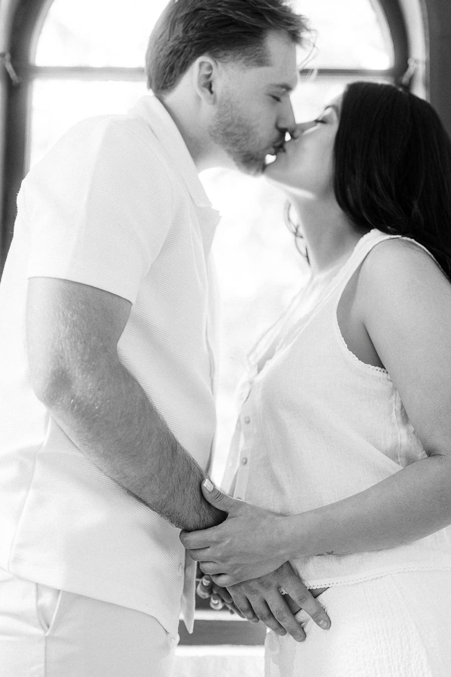Couple kissing and holding hands in a black and white engagement photo.
