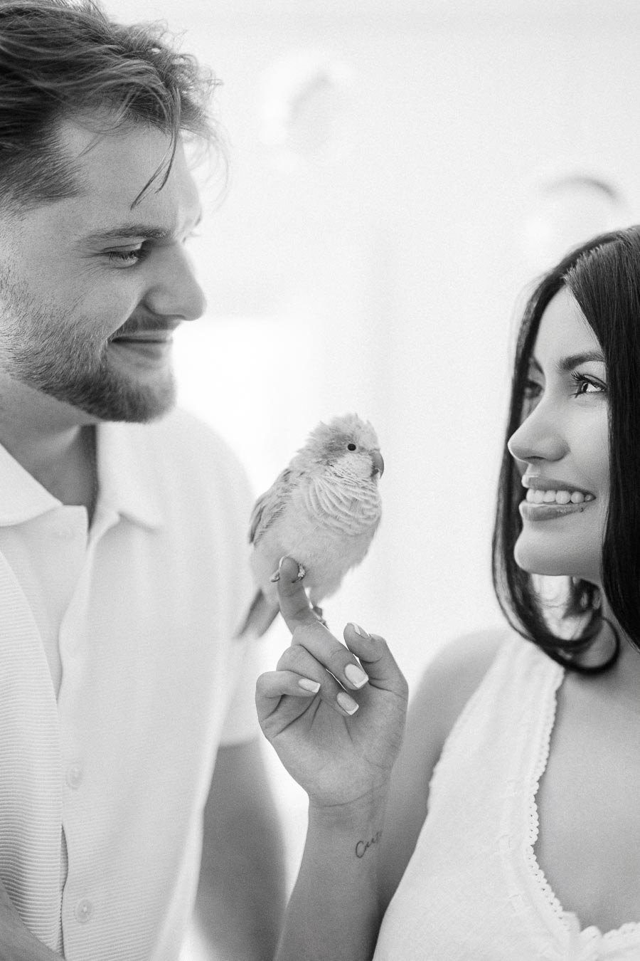 Couple smiling at each other while a small bird perches on her finger.