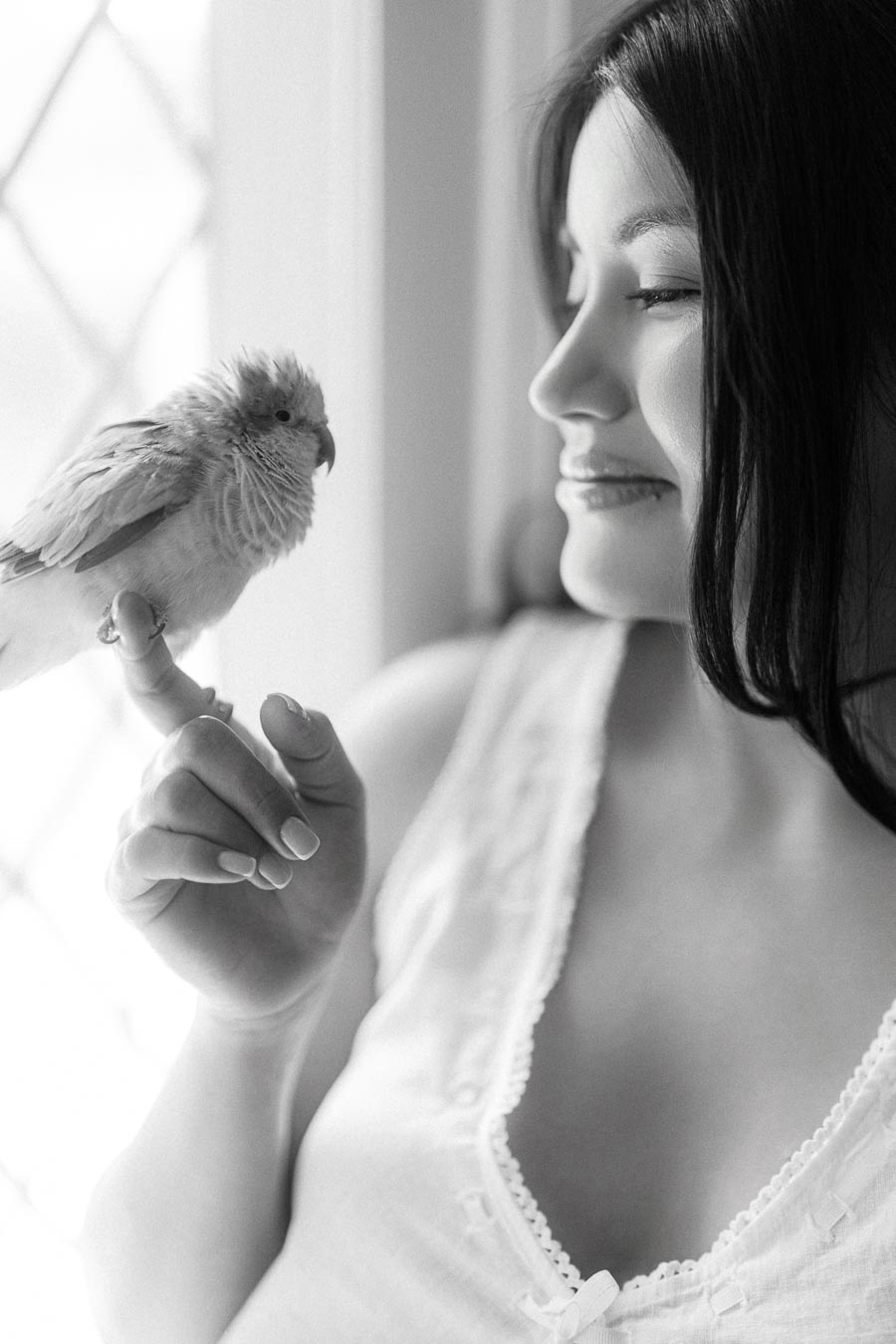 Woman in a white top holding a small bird near a bright window.
