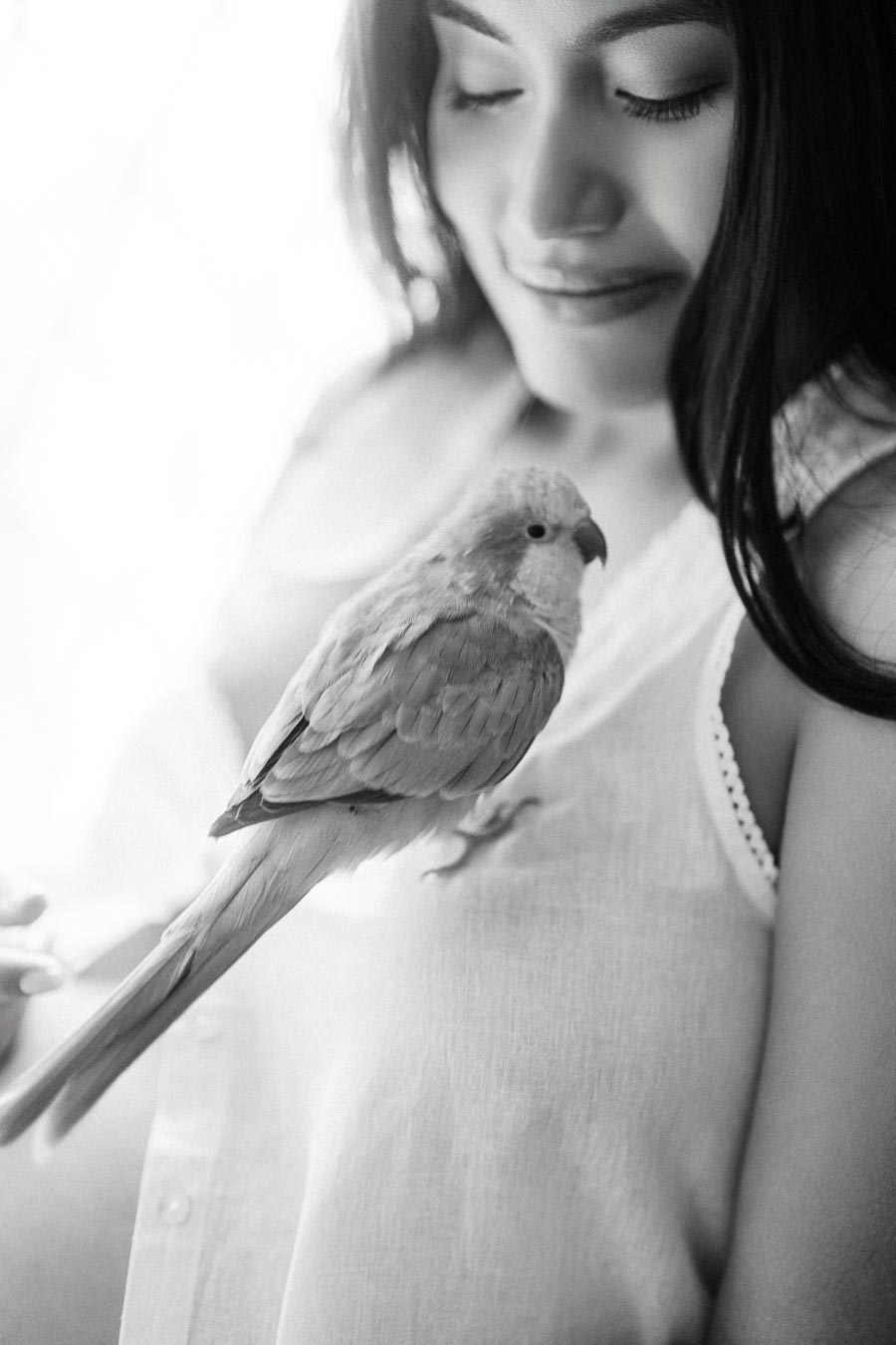 Black and white close-up of a woman looking down at a small bird.
