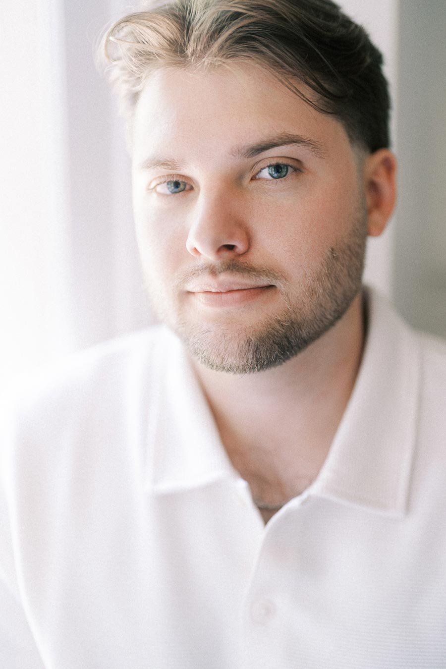 Close-up engagement portrait of a man in a white shirt by a window.