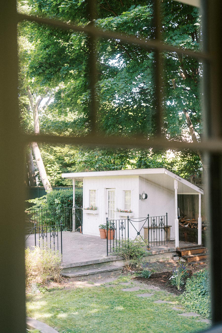 Garden view through a window showing a small white cottage and trees.