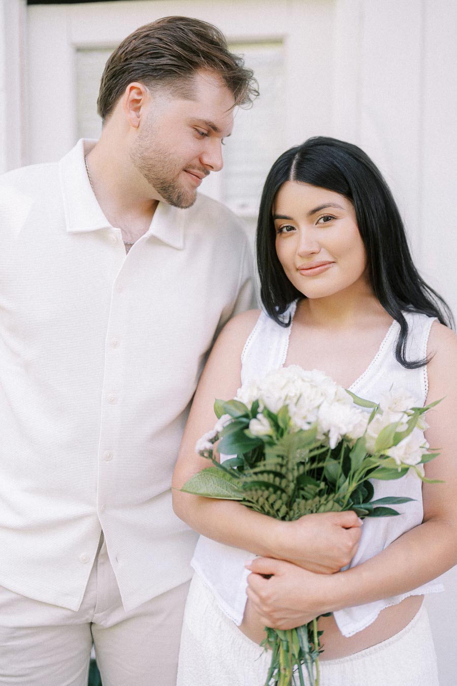 Engaged couple in white outfits posing with a bouquet during a Toronto engagement photo.