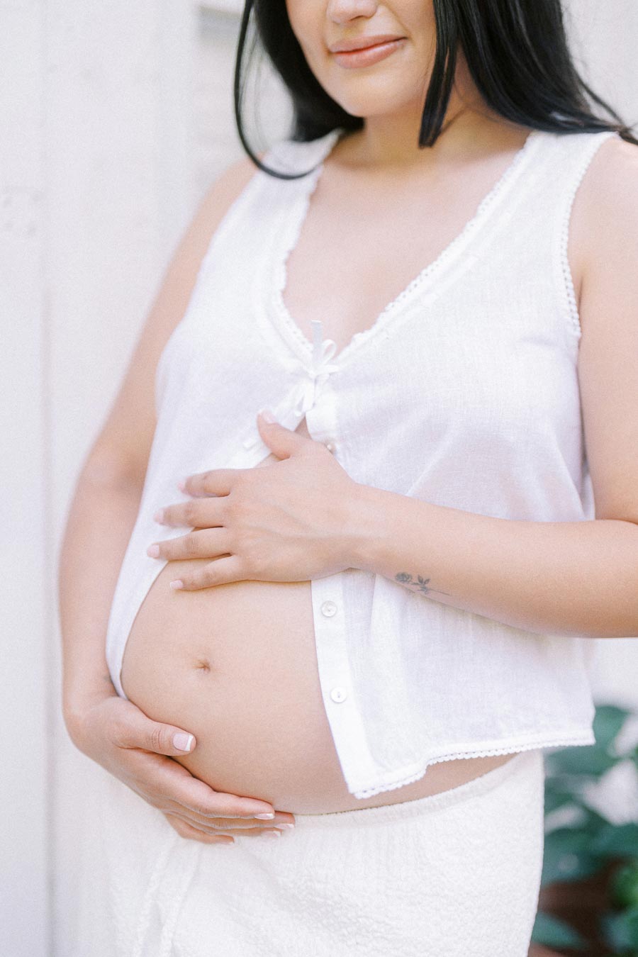 Pregnant woman in white clothing gently holding her belly.