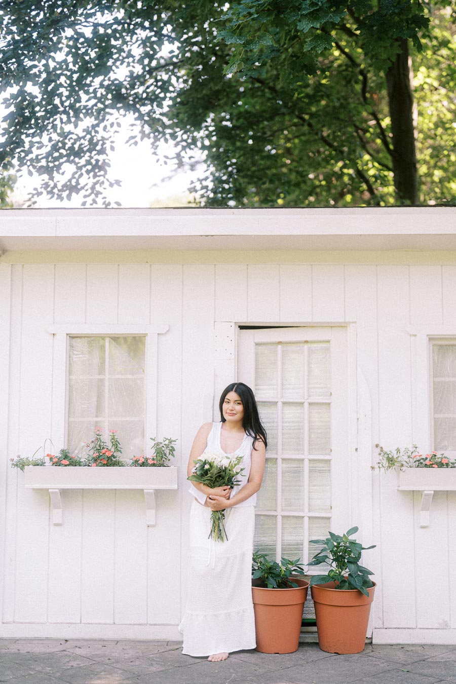 Woman in a white dress holding a bouquet outside a white garden building.
