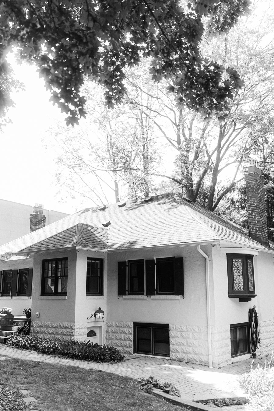 Black and white view of a small house beneath leafy trees.
