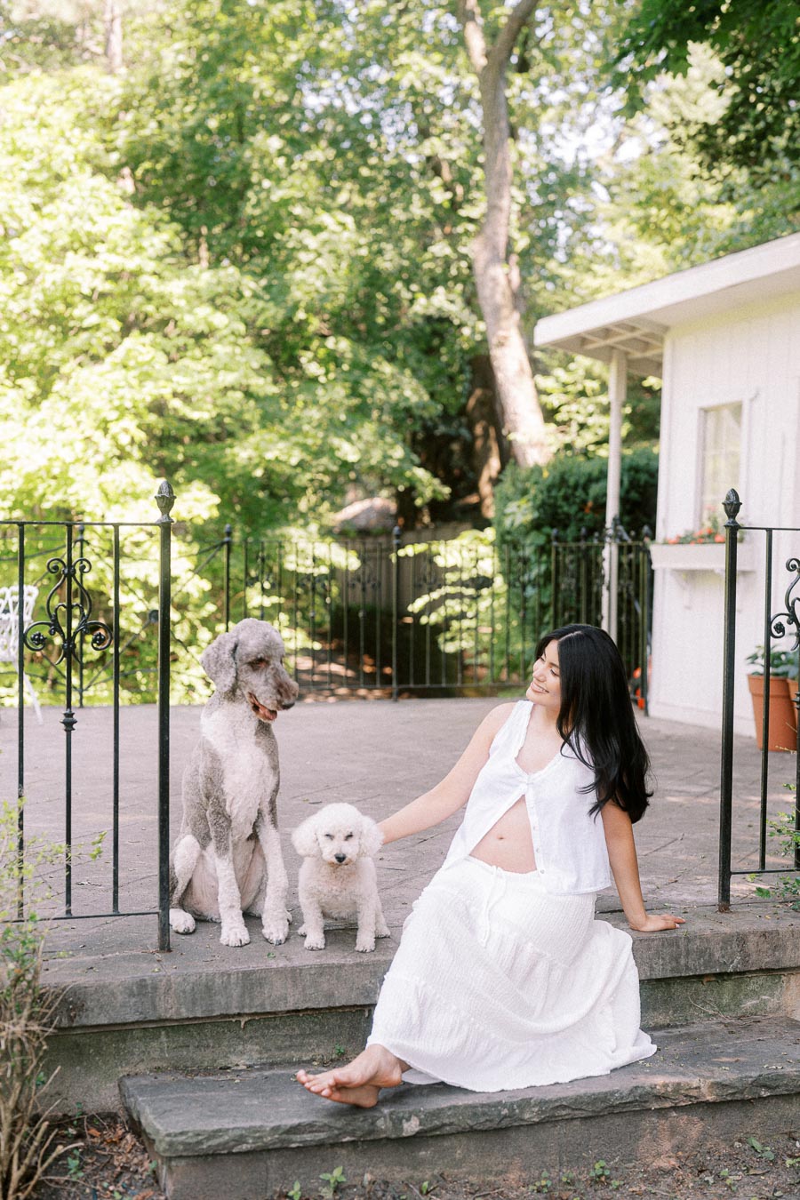 Woman in a white dress sitting on stone steps with two dogs.