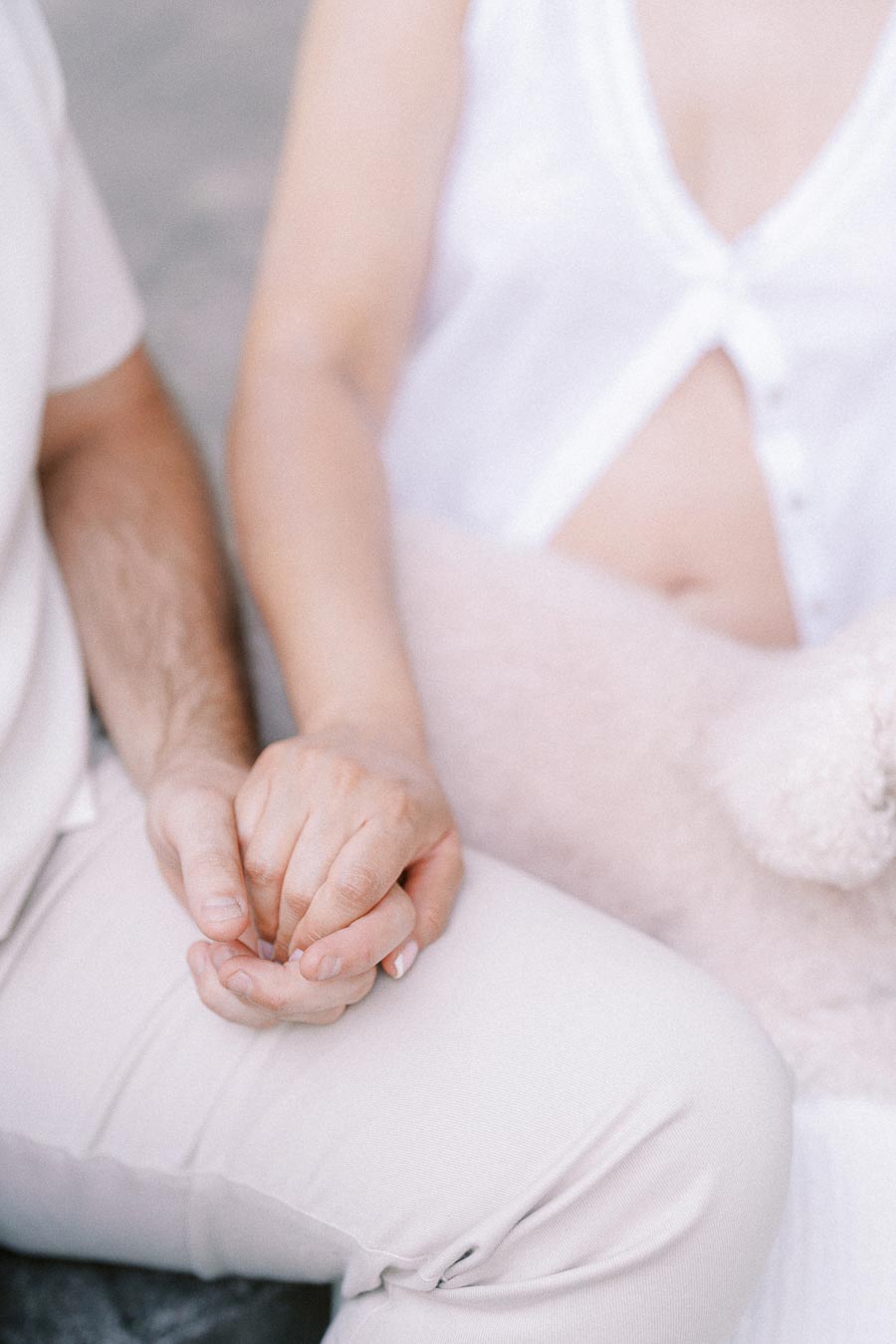 Close-up engagement photo of a couple gently holding hands in light clothing.