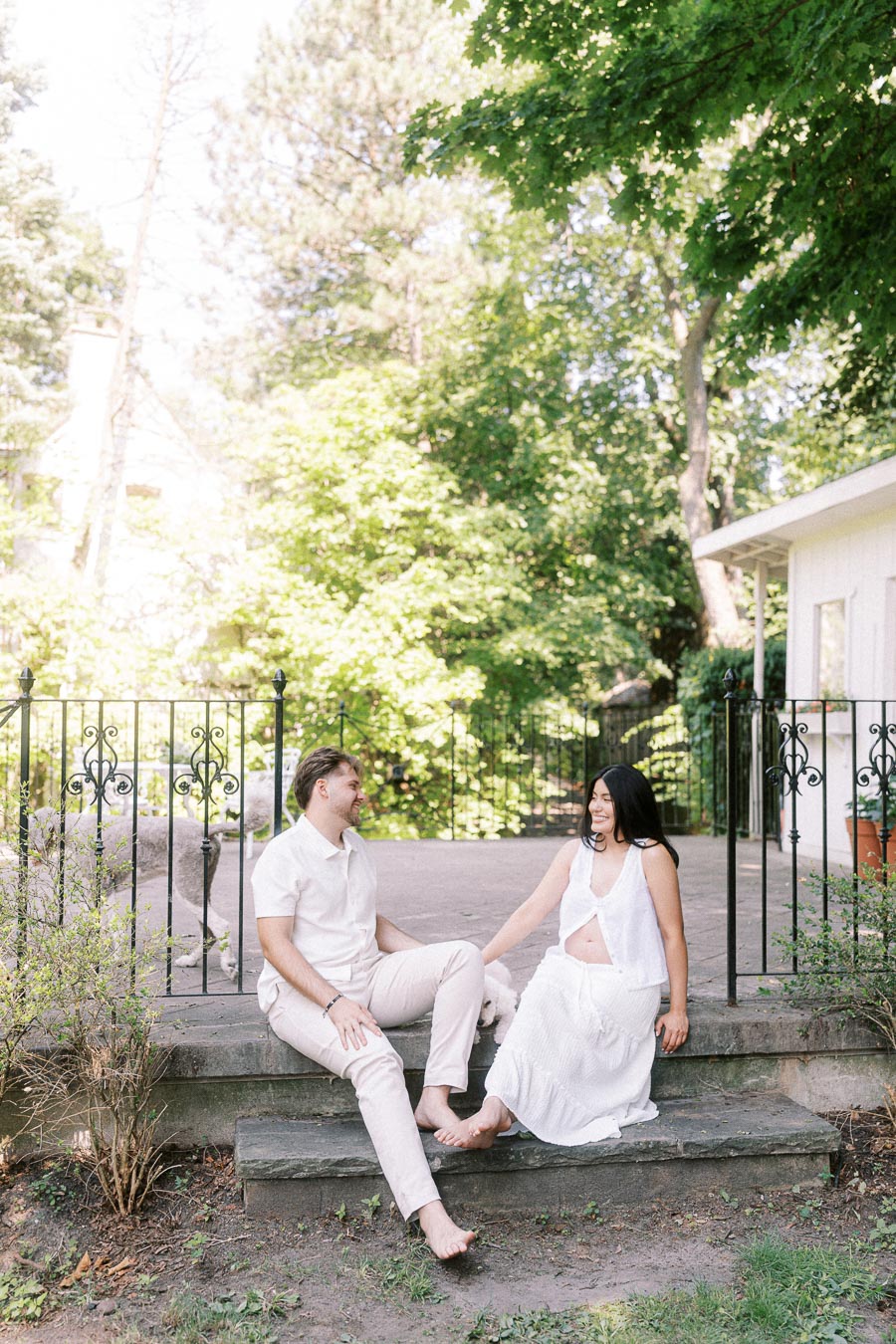 Engaged couple sitting barefoot on stone steps in a leafy Toronto garden.